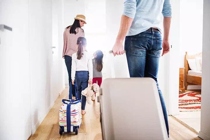 Family of four walking out of their home with suitcases